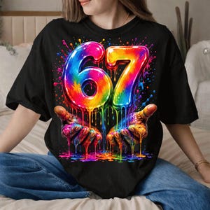 Może przedstawiać: Czarny t-shirt z kolorową grafiką przedstawiającą liczbę "67" w tęczowym wzorze, z efektami spływającej farby. Projekt zawiera dwie dłonie trzymające spływającą farbę. Koszulka jest w stylu casual.