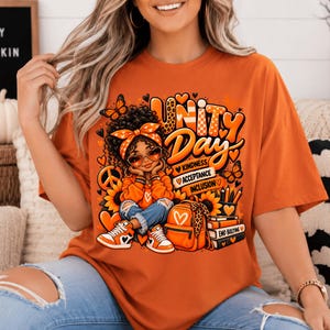 Puede incluir: Una camiseta naranja con un gráfico de una persona con cabello rizado que lleva una diadema, gafas de sol y una sudadera naranja. El diseño incluye el texto Unity Day, Kindness, Acceptance, Inclusion y End Bullying, con girasoles, mariposas, corazones, una mochila y libros.