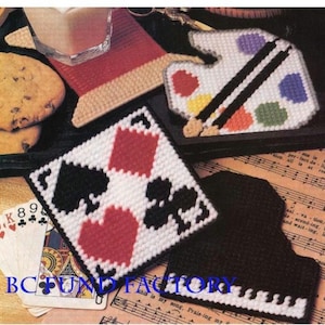 Może przedstawiać: Kolekcja ręcznie robionych podkładek. Jedna z nich przedstawia wzór kart do gry z sercami, pikami, treflami i karami. Inna ma kształt palety malarskiej z kolorami i pędzlami. Trzecia podkładka ma kształt fortepianu.