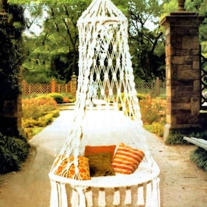 Peut inclure: Une chaise suspendue en macramé blanc dotée d'une base circulaire avec des pompons décoratifs. Le siège est agrémenté de trois coussins carrés de couleur orange unie, vert olive uni et à rayures horizontales orange et blanches.