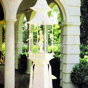 May include: A white macramé hanging structure titled Macramé Enchantment Book 4, featuring a tiered pagoda-style top, a central figurine, and a base with long fringe. The text Fountain of the Orient is printed at the bottom of the image.