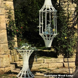 May include: A white macrame table and hanging lamp with a decorative birdcage design. The lamp features a small figurine and several bird accents. The table has a glass top. The text "Norwegian Wood Lamp and Table" is visible.