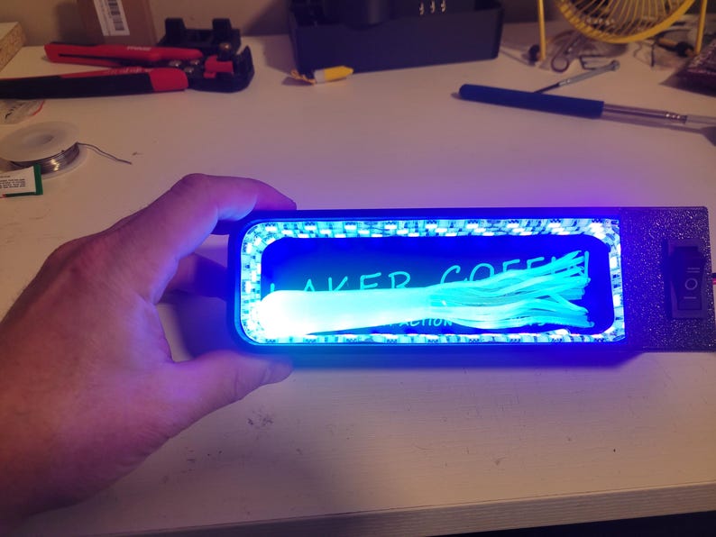 May include: A rectangular device with a blue LED light frame, illuminating a blue interior with the text "LAKER COFFEE" and a bundle of light blue fibers. A switch is on the right side.