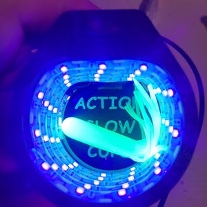 May include: A close-up of a black device with a blue LED light ring. The center displays the words "ACTION SLOW CUT" in white. A glowing green fiber optic bundle extends from the center.