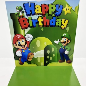 Puede incluir: Tarjeta de cumpleaños verde y azul con los personajes de Mario y Luigi. La tarjeta tiene las palabras "Happy Birthday" en letras grandes y coloridas. También se ve un personaje verde de Yoshi.
