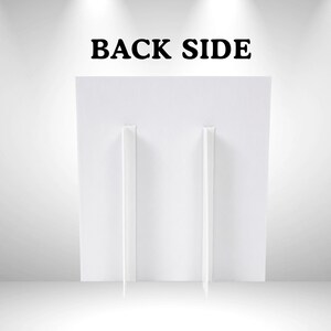 以下が含まれることがあります： 上部に黒い大文字でBACK SIDEと書かれた白い長方形のディスプレイボード。ボードの背面には2つの垂直な白い段ボール製のイーゼルスタンドが取り付けられており、直立した状態で安定感を保つ構造になっています。