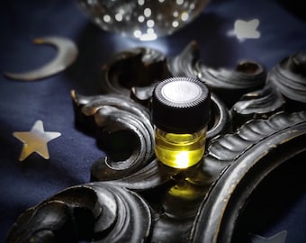 Puede incluir: Una pequeña botella de vidrio transparente con una tapa negra llena de un líquido dorado. La botella está sentada sobre un marco negro adornado con un fondo azul.