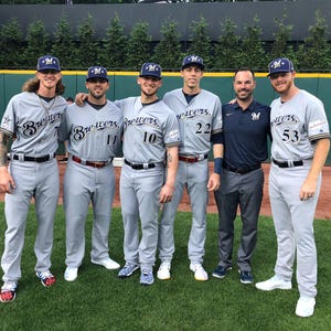 Könnte beinhalten: Eine Gruppe von Baseballspielern und ein Trainer in grauen und marineblauen Uniformen. Die Spieler tragen graue Baseballkappen mit einem blauen "M"-Logo. Die Uniformen tragen den Schriftzug "Brewers". Der Trainer trägt ein marineblaues Poloshirt mit demselben Logo.