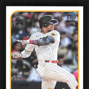 May include: A baseball card featuring Juan Soto of the San Diego Padres. The card has a yellow and brown Padres logo, with the player's name at the bottom. The player is wearing a white and brown striped uniform and a black helmet.