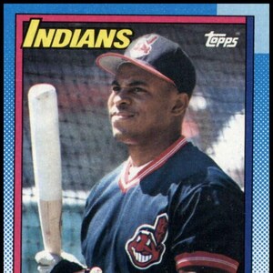 Può includere: Carta di baseball con Joey Belle dei Cleveland Indians. La carta ha un bordo blu, rosso e giallo. Il giocatore indossa una maglia blu navy con il logo della squadra e tiene una mazza da baseball. La parola "Indians" è in alto.