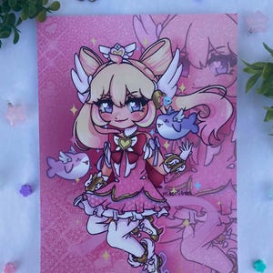 Peut inclure: Une impression d'art rose représentant un personnage de dessin animé aux cheveux blonds, des ailes et une couronne. Le personnage porte une robe rose et est accompagné de deux poissons bleus. Le fond est rose avec un effet pailleté. La signature de l'artiste est visible.