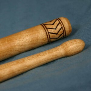 May include: Two wooden drumsticks, one with a decorative black and white chevron pattern near the top.