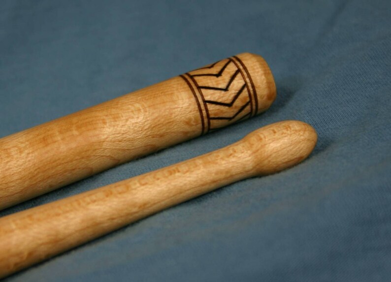 May include: Two wooden drumsticks, one with a decorative black and white chevron pattern near the top.