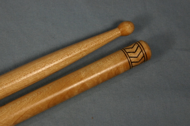 May include: Two wooden drumsticks, one with a plain round tip and the other with a decorative black chevron pattern near the tip.