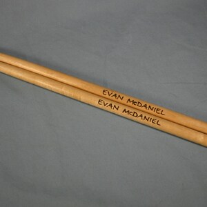 May include: A pair of wooden drumsticks with the name "Evan McDaniel" engraved on them.