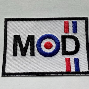 May include: Embroidered patch with the word "MOD" in black block letters. The "O" is a blue circle with a red center. Red and blue vertical stripes flank the "D". The patch has a white background and a black border.