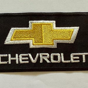 May include: Black rectangular patch featuring the Chevrolet logo, a gold bow tie emblem with a white outline. The word "CHEVROLET" is embroidered in white block letters below the logo. The patch has a black border.