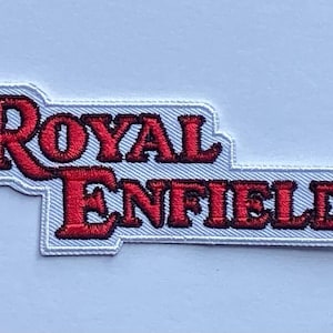 May include: Embroidered patch featuring the words "Royal Enfield" in red, outlined in white. The patch has a rectangular shape with a unique, layered design. The text is in a bold, stylized font, suitable for application on clothing or accessories.