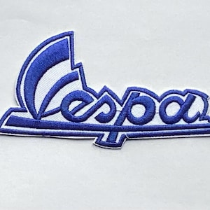 Può includere: Toppa ricamata con la scritta "Vespa" in blu su sfondo bianco. Il design include una forma curva sopra la parola e una forma rettangolare sotto. Ideale per abbigliamento o accessori.