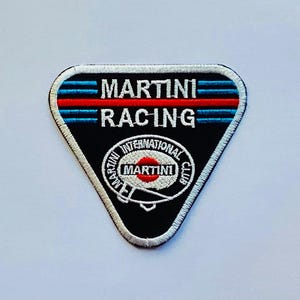 May include: A triangular black patch with the words "MARTINI RACING" in white. The patch has blue and red stripes at the top and a circular logo with the words "MARTINI INTERNATIONAL CLUB". The patch is outlined in white.