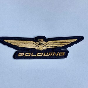 May include: Embroidered patch with a gold wing design and the word "GOLDWING" in gold lettering on a navy blue background. The patch has a detailed, textured appearance.