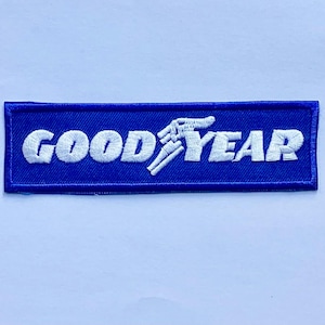 May include: A rectangular embroidered patch featuring a vibrant blue background with the word GOODYEAR stitched in white thread. The text includes the iconic winged foot logo integrated into the letter Y, with a clean stitched border.