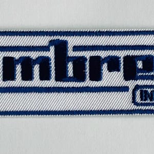 May include: A rectangular patch with the word "Lambretta" in dark blue, stylized text. The patch has a white background with blue borders and the word "Innocenti" in a smaller font. The patch is likely for a scooter or vintage vehicle.