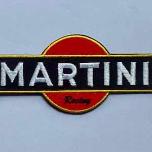 Könnte beinhalten: Gestickter Aufnäher mit dem Logo "MARTINI Racing". Das Design umfasst ein schwarzes Rechteck mit dem Wort "MARTINI" in Weiß, vor einem roten Kreis und einem goldenen Rand. Das Wort "Racing" ist rot.