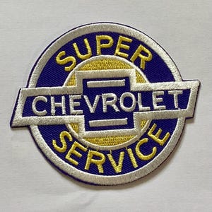 Può includere: Toppa ricamata con un design circolare con le parole "SUPER CHEVROLET SERVICE" in lettere gialle e bianche su sfondo blu. Il logo Chevrolet è ben visibile al centro.