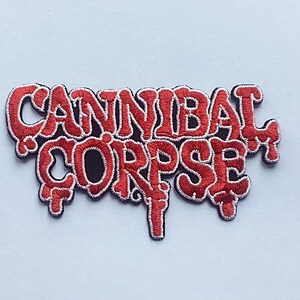 May include: Embroidered patch featuring the band name "CANNIBAL CORPSE" in red, stylized lettering with a dripping effect. The patch has a black background and a white border, set against a light blue backdrop.