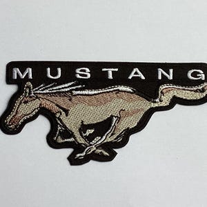 May include: Embroidered patch with the word "MUSTANG" above a running horse. The patch has a black background with white lettering. The horse is tan and brown with white detailing.
