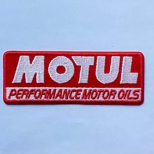 May include: A rectangular embroidered patch featuring a red background with the white text MOTUL in a bold font. Below the brand name, the text PERFORMANCE MOTOR OILS is embroidered in red on a white horizontal stripe across the bottom section.