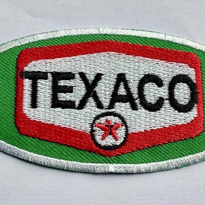 May include: Embroidered Texaco patch in an oval shape. The patch features a green background with a white border. The center has a red and white design with the word "TEXACO" in black and a red star.