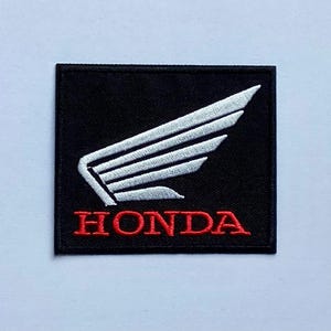 Puede incluir: Parche cuadrado negro con el logotipo de Honda. El logotipo incluye un diseño de ala blanca y la palabra "HONDA" en rojo, bordada sobre un fondo negro. Ideal para ropa o accesorios.