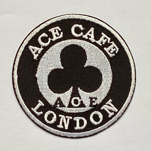 Puede incluir: Parche bordado circular en blanco y negro con el texto "ACE CAFE LONDON". El parche presenta un diseño blanco en forma de trébol en el centro. El texto está en negrita, sin serifa.