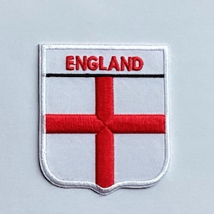 May include: Embroidered England flag patch. The patch has a white background with a red cross and the word "ENGLAND" in red letters at the top. The patch is bordered with a silver trim.