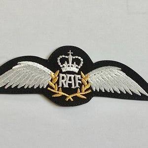 Puede incluir: Parche bordado con fondo negro, alas blancas y una corona. Las letras "RAF" están en el centro, rodeadas por una corona dorada. Un emblema clásico.