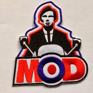 Può includere: Toppa ricamata con un design Mod. Presenta una figura in abito nero su uno scooter, con la parola "MOD" in rosso. La toppa ha una combinazione di colori rosso, bianco e blu, con un contorno bianco e blu.