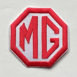 Könnte beinhalten: Gestickter Aufnäher mit den Buchstaben "MG" in Rot auf weißem Grund, umrahmt von einem roten achteckigen Rand. Der Aufnäher hat eine genähte Textur, die für das Aufnähen auf Kleidungsstücke oder Accessoires geeignet ist.