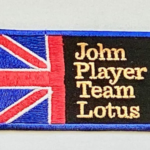 May include: Embroidered patch featuring the Union Jack flag and the text "John Player Team Lotus" in gold lettering on a black background. The patch has a blue border.