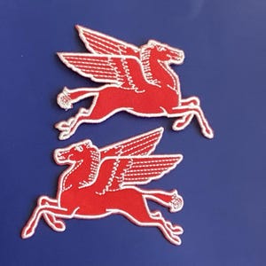 May include: Two red embroidered patches of a winged horse, also known as a Pegasus, on a blue background. The patches are detailed with white stitching, depicting the horse in a running pose with outstretched wings.