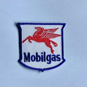 Op de afbeelding: Geborduurde Mobilgas-patch met een rode Pegasus op een witte achtergrond. De patch heeft een blauwe rand en het woord "Mobilgas" in blauwe letters. Een klassiek auto-embleem.