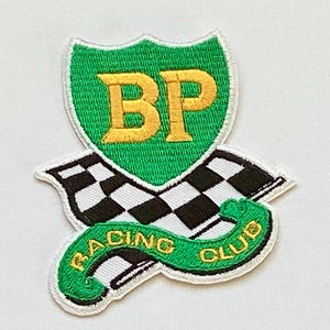 May include: Embroidered patch featuring a green shield with the letters "BP" in gold. Below the shield is a black and white checkered flag and a green banner that reads "RACING CLUB" in gold lettering. The patch has a white border.