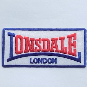 May include: Embroidered patch with the name "LONSDALE" in red, arched above "LONDON" in blue. The text is on a white background, framed by a blue border. A classic logo for clothing.