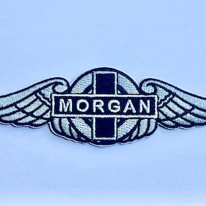 Op de afbeelding: Geborduurde patch met een gevleugeld ontwerp en de naam "MORGAN". De vleugels zijn lichtblauw met zwarte contouren en de tekst is wit. De patch heeft een zwart-wit kleurenschema.