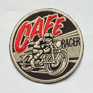 May include: Round embroidered patch featuring a motorcycle racer on a vintage bike. The patch has a black background with the words "CAFE RACER" in red and white. The patch is bordered with a tan thread.