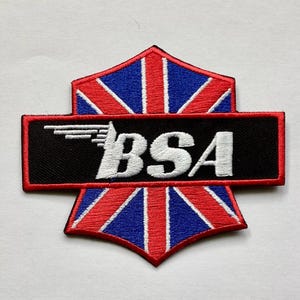 Può includere: Toppa ricamata con le lettere "BSA" in bianco su sfondo rettangolare nero con ali stilizzate. La toppa è incorniciata da un design rosso, bianco e blu che ricorda la bandiera Union Jack.