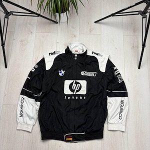 May include: Black and white racing jacket with sponsor logos, including "FedEx" and "HP invent." The jacket features a stand-up collar, ribbed cuffs, and a BMW logo. The sleeves have white panels and the text "NiQutinCQ."
