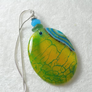 May include: A green, yellow, and blue agate pendant with a silver chain. The pendant has a cracked, textured surface and is oval shaped.