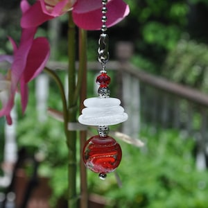 May include: A red and white glass ceiling fan pull chain with a silver chain and beads. The chain has a red glass bead, a stack of three white glass beads, and a red glass orb.